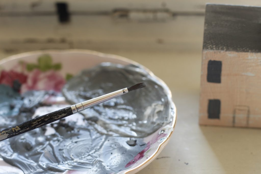 image of plate holding gray paint and a paintbrush resting on the plate and a small painted house in the background
