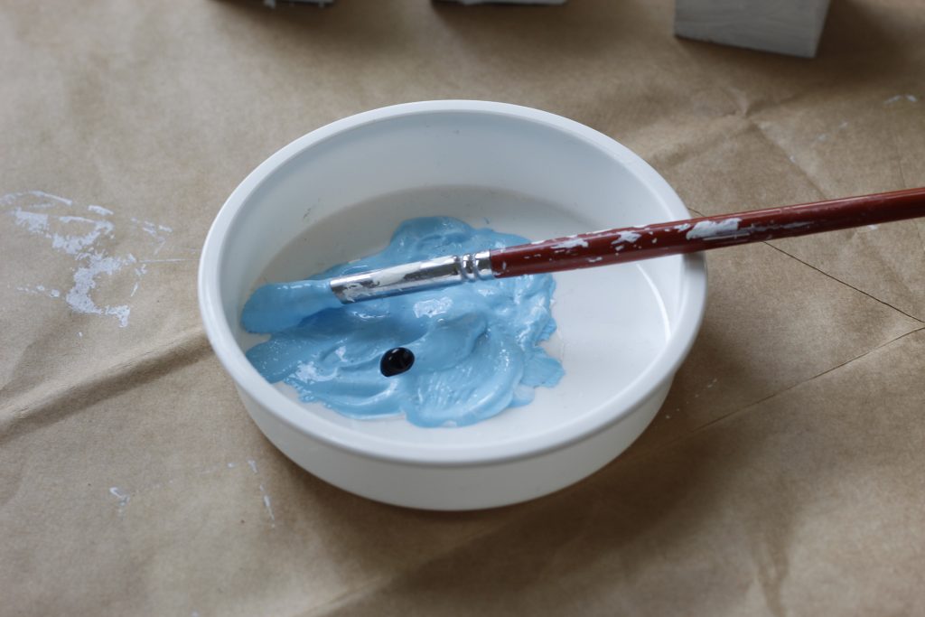 image of blue paint and a dab of black paint in a dish with a paintbrush