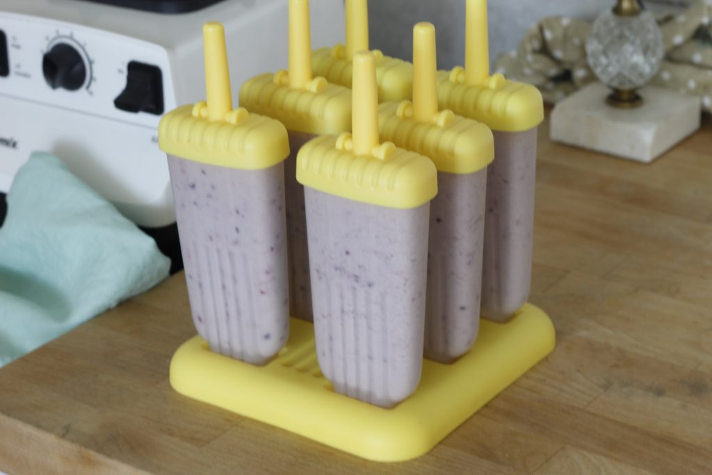 close-up picture of popsicle mold full of coconut berry kombucha  popsicle mixture on a wooden counter beside a white blender