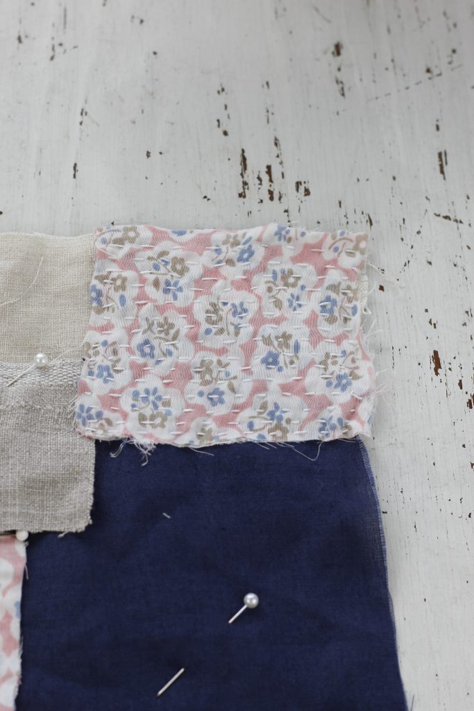 image of floral pink fabric with running stitches on top of blue and beige linen fabric lying on a white table