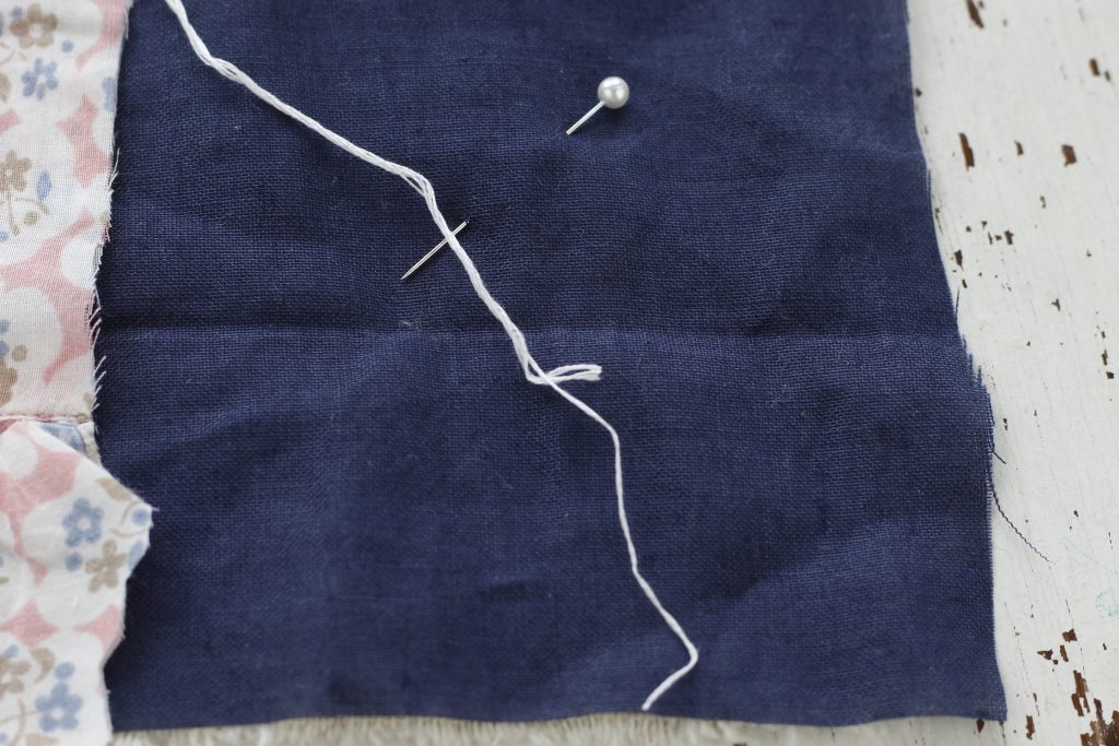 image of floral fabric and blue fabric with a pin and white thread  two threads are partially pulled out