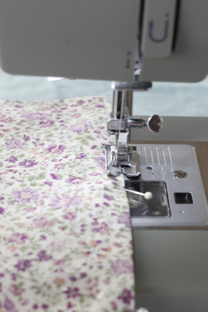 close-up picture of a seam being sewn on the purple floral fabric on a sewing machine