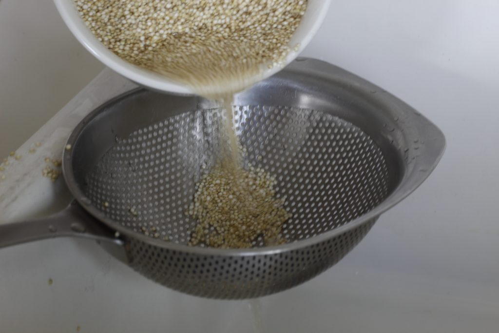 image of soaked quinoa being poured into a metal colander over a white sink