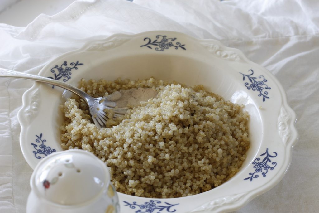 image of soaked and cooked quinoa in a white dish with blue flowers on a white tablecloth and a piece of white china in the foreground