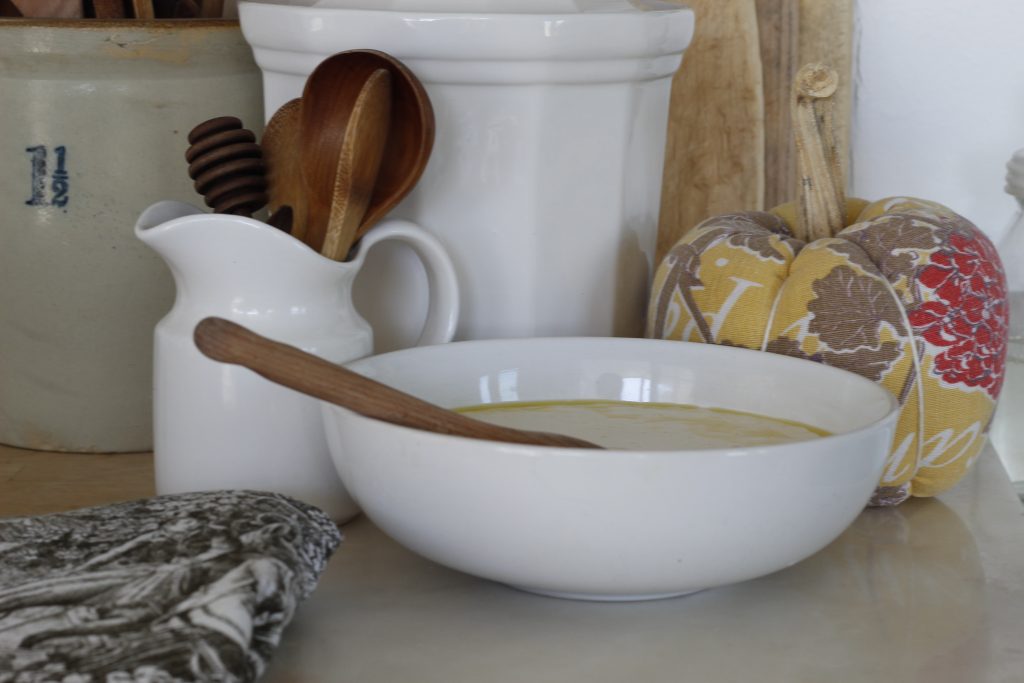 image of bowl of sourdough and wooden spoons with various white and beige crocks in the background and  a brown and white towel in the foreground