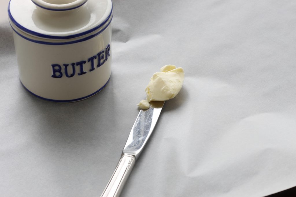 image of butter dish and butter on knife lying on a parchment paper lined baking sheet