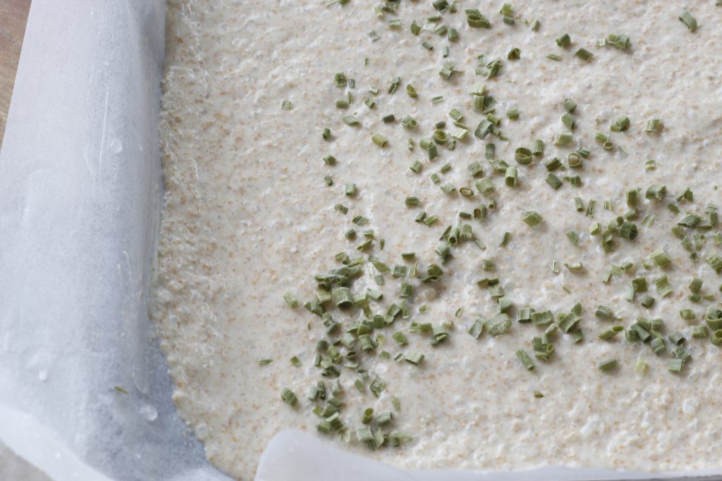 image of rice and sourdough discard cracker dough on a baking sheet sprinkled with chives