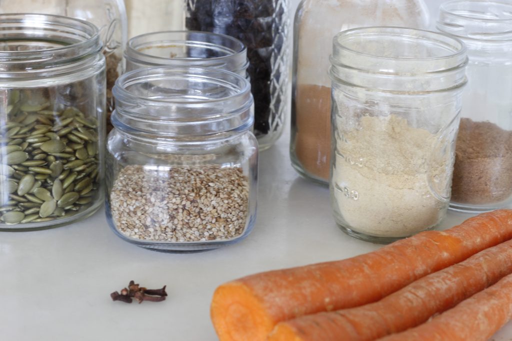 image of ingredients in jars lined up on a kitchen counter and carrots lined up in the foreground