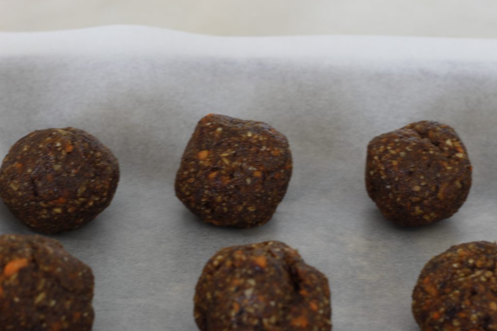 close up image of spicy carrot cake snack bites lined up on a parchment lined baking pan