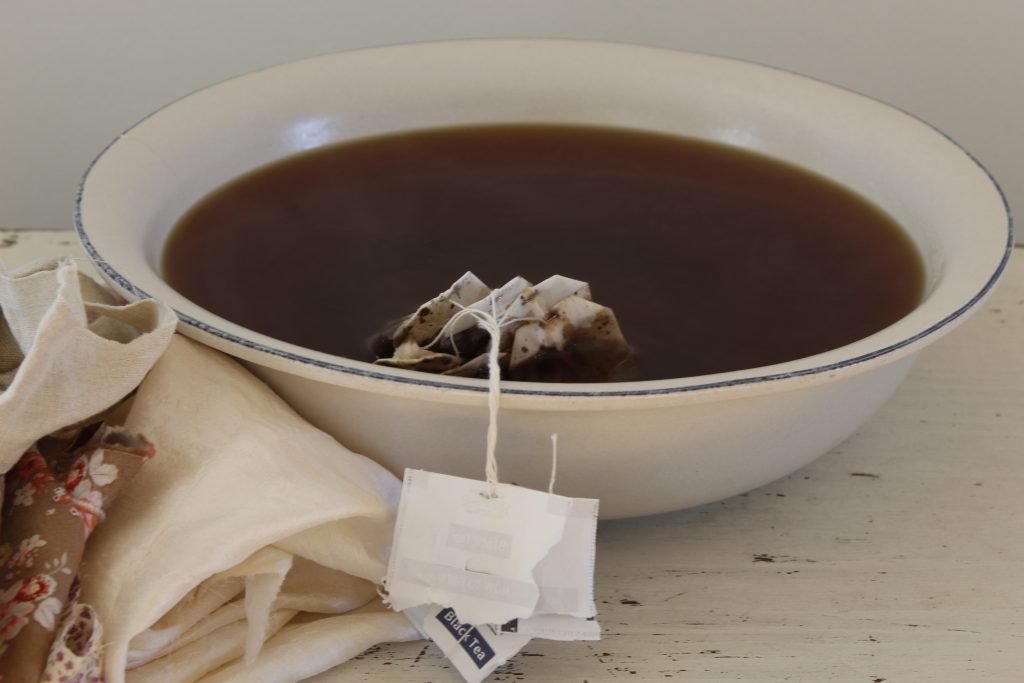 image of tea-dye steeping in a large blue and white bowl on a white table next to a pile of fabric