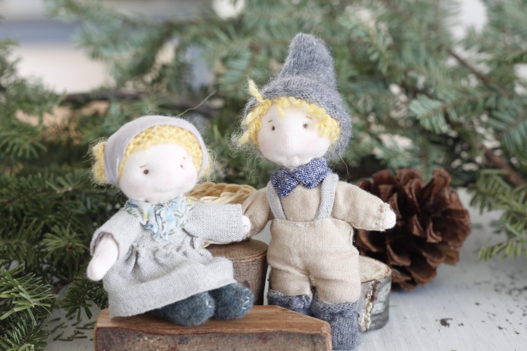 image of Hansel and Gretel dolls dressed in linen clothes standing and sitting by evergreen branches