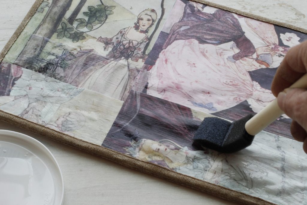 picture showing hand using a foam brush to apply sealant to the surface of the fairy tale picture covered mousepad showing strokes in one direction