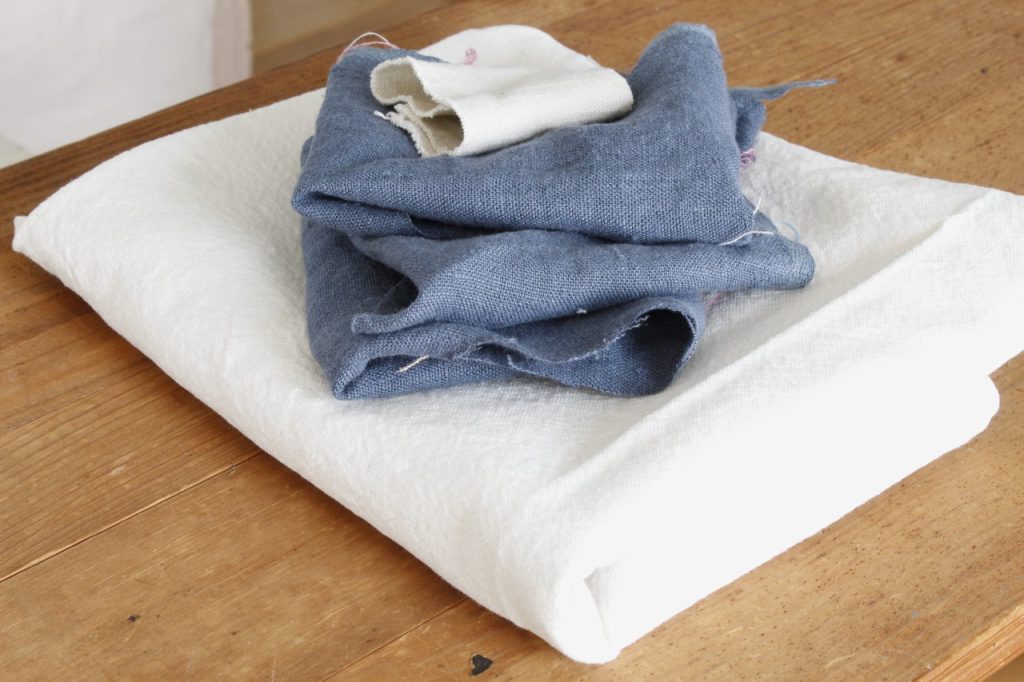 image of white fabric and blue fabric piled neatly on a wooden ironing board