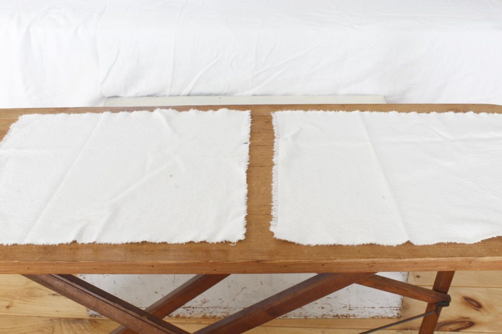 This image shows two pieces of ivory colored fabric that have been cut out, lying on a brown wooden ironing board.