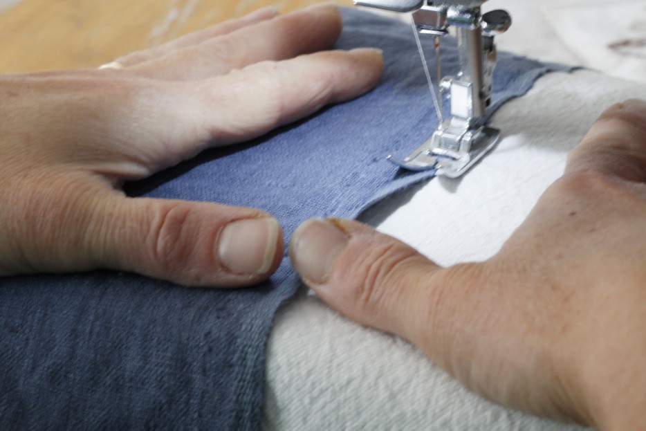 This is an image of hands holding the sewing project and guiding it into the sewing machine as it sews it together.