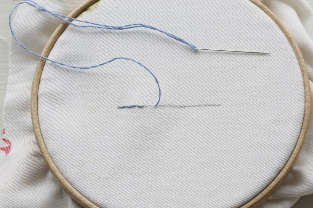 This image is showing a backstitch on a white fabric with blue thread.
