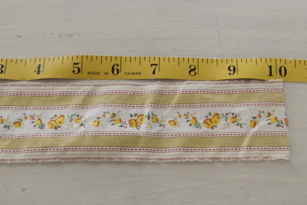 This is an image of a scrap of floral yellow fabric lying on a white table being measured with a yellow tape measure.
