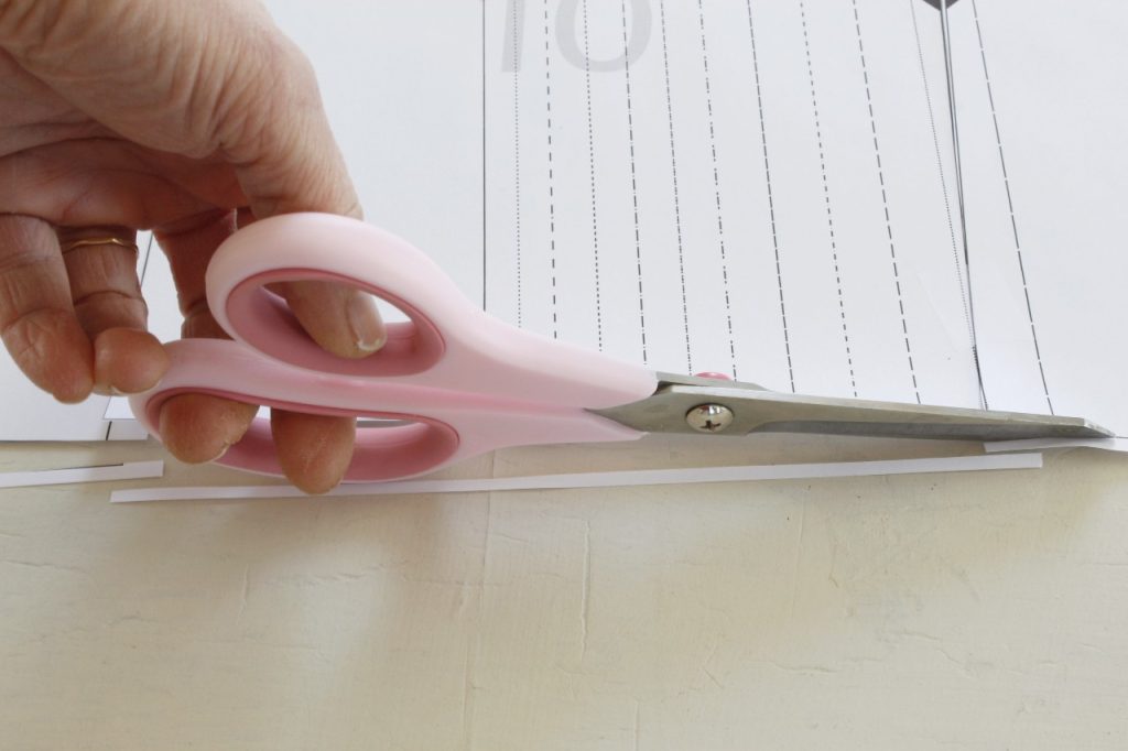 This is an image of a hand holding pink scissors and cutting a strip of paper off the sewing pattern, showing the assembly process in action.