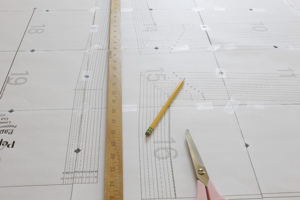 This is an image of a yard stick being used to mark a line to separate the two long halves of the PDF sewing pattern. There is also a yellow pencil and scissors lying on the pattern.