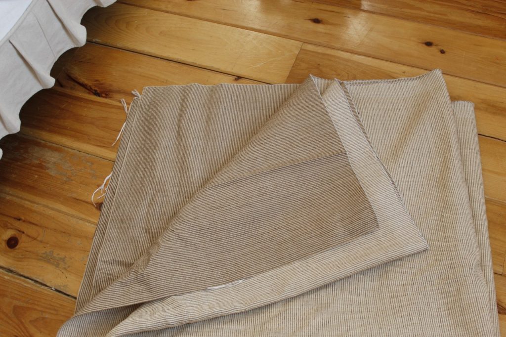 This image shows beige fabric folded and lying on a wooden floor.