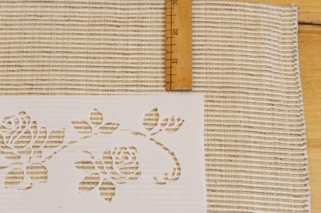 This image shows a ruler measuring three inches from the edge and the stencil is placed that distance to prepare to paint the rug.