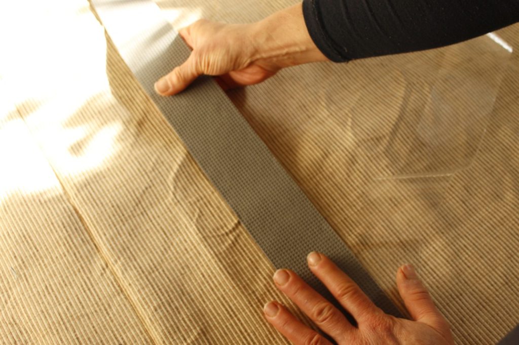 This image shows the woman's hands sticking the rug tape to the back of the handmade rug.