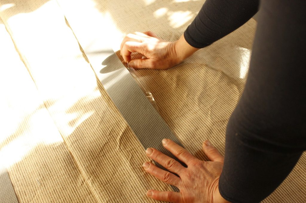 This image shows a woman's hands pulling the backing strip from the back of the rug tape in order to adhere the rug tape.
