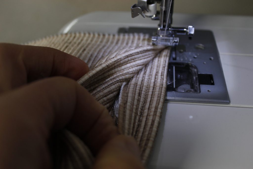 This image shows a hand guiding the fabric through a sewing machine as it is being sewn.