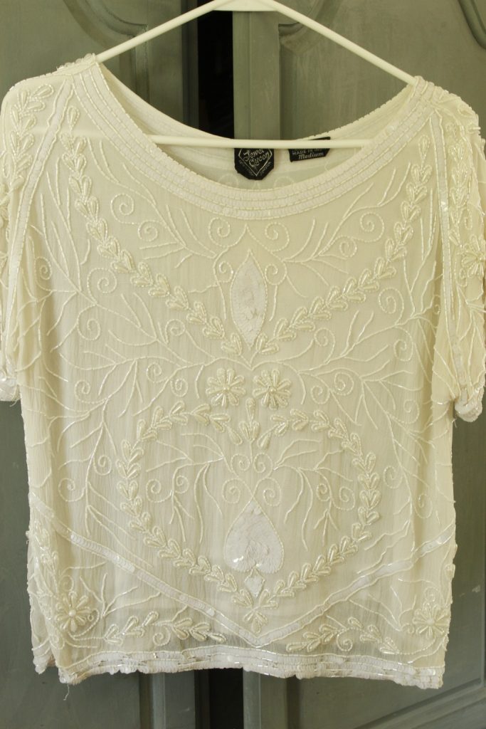 This image shows a white silk beaded and sequined women's top hanging on a hanger, this shows the top that will be embellished with the natural dyed silk fabric.