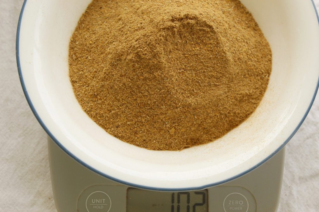 This image shows the dried symplocos powder in a bowl being weighed on a digital scale.