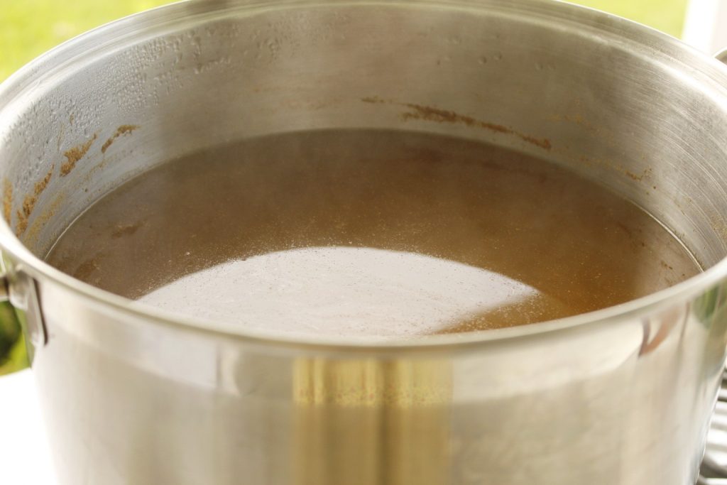This image shows a large stainless steel dye pot with brown liquid which is the mordant symplocos simmering to prepare to mordant the silk fabric.